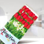 Caja transparente con 18 rosas rojas y flores blancas sobre fondo de interior desenfocado