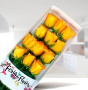 Caja rectangular blanca con doce rosas amarillas en botón sobre fondo interior desenfocado