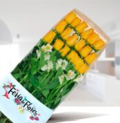 Caja rectangular con 18 rosas amarillas alineadas y flores blancas sobre fondo desenfocado