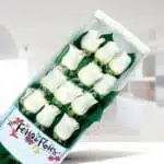 Caja rectangular con 12 rosas blancas sobre fondo verde y logo Feria de Flores