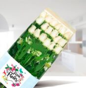 Caja transparente con 18 rosas blancas y follaje verde de Feria de Flores