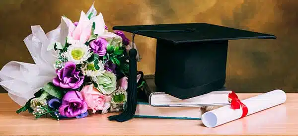 Ramo de flores de colores junto a un birrete de graduación negro y un diploma enrollado sobre una mesa de madera