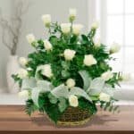 Arreglo floral de rosas blancas en canasta de mimbre sobre mesa de madera