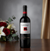 Botella de vino tinto GatoNegro Cabernet Sauvignon sobre una mesa de madera con ramo de rosas rojas y lirios blancos desenfocado al fondo