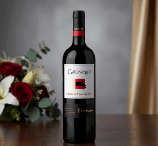 Botella de vino tinto GatoNegro Cabernet Sauvignon sobre una mesa de madera con ramo de rosas rojas y lirios blancos desenfocado al fondo