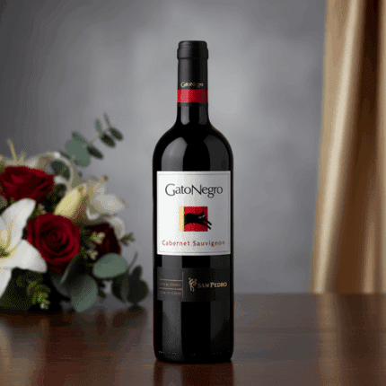 Botella de vino tinto GatoNegro Cabernet Sauvignon sobre una mesa de madera con ramo de rosas rojas y lirios blancos desenfocado al fondo