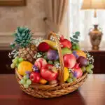 Canasta de mimbre llena de frutas variadas como piña, manzanas, uvas, plátano, granada, cítricos y flores decorativas sobre una mesa de madera en interior elegante