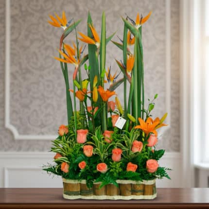 Arreglo floral alto con aves del paraíso y rosas naranjas en base de bambú sobre mesa interior