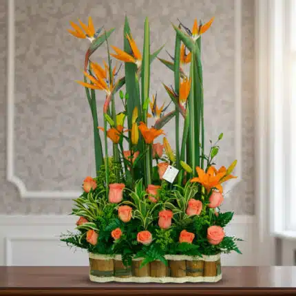 Arreglo floral alto con aves del paraíso y rosas naranjas en base de bambú sobre mesa interior