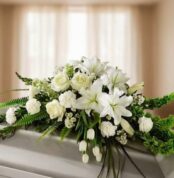 Centro de flores blancas con lirios, rosas y claveles sobre un ataúd en una sala iluminada