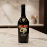 Botella de licor Baileys The Original Irish Cream negra sobre encimera de mármol en cocina desenfocada