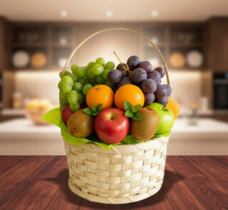 Cesta tejida de mimbre llena de frutas variadas como uvas verdes y moradas, manzanas rojas, naranjas, kiwi y peras sobre una mesa de madera con una cocina desenfocada de fondo