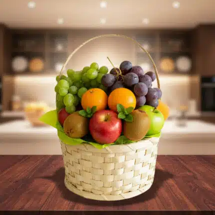 Cesta tejida de mimbre llena de frutas variadas como uvas verdes y moradas, manzanas rojas, naranjas, kiwi y peras sobre una mesa de madera con una cocina desenfocada de fondo