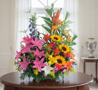 Arreglo de flores variadas con girasoles, lirios rosados y aves del paraíso sobre una mesa redonda de madera en una sala luminosa