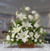 arreglo de flores blancas con lirios y claveles en una canasta de mimbre sobre mesa de madera