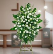 Arreglo floral grande de rosas y flores blancas con follaje verde sobre caballete metálico en interior