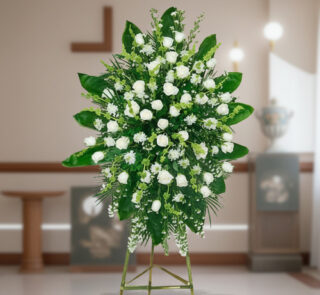 Arreglo floral grande de rosas y flores blancas con follaje verde sobre caballete metálico en interior