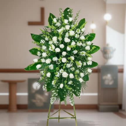 Arreglo floral grande de rosas y flores blancas con follaje verde sobre caballete metálico en interior