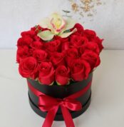Arreglo floral de rosas rojas en caja redonda negra con lazo rojo y una orquídea blanca en la parte superior