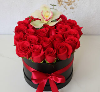 Arreglo floral de rosas rojas en caja redonda negra con lazo rojo y una orquídea blanca en la parte superior