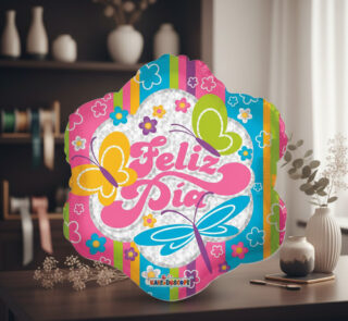 Globo decorativo de colores con texto Feliz Día, mariposas y flores sobre una mesa de madera en una sala con estantería y jarrones al fondo