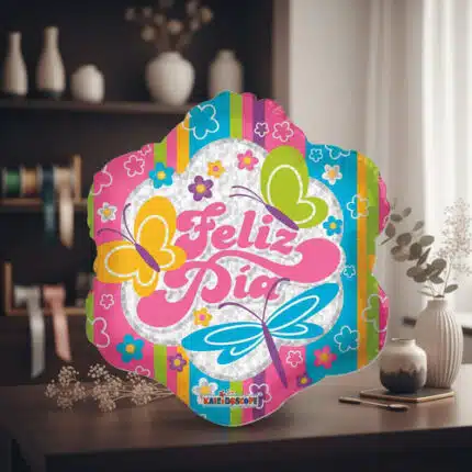 Globo decorativo de colores con texto Feliz Día, mariposas y flores sobre una mesa de madera en una sala con estantería y jarrones al fondo