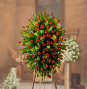 arreglo floral funerario de rosas rojas y hojas verdes sobre caballete de madera en el interior de una iglesia desenfocada