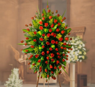 arreglo floral funerario de rosas rojas y hojas verdes sobre caballete de madera en el interior de una iglesia desenfocada