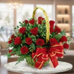 Arreglo floral de rosas rojas en canasta de mimbre con lazo rojo y dorado sobre mesa de mármol