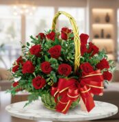Arreglo floral de rosas rojas en canasta de mimbre con lazo rojo y dorado sobre mesa de mármol