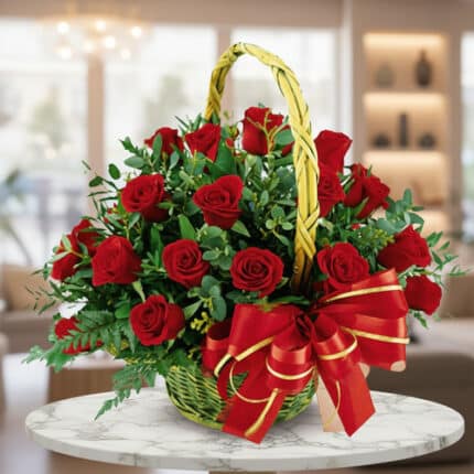 Arreglo floral de rosas rojas en canasta de mimbre con lazo rojo y dorado sobre mesa de mármol