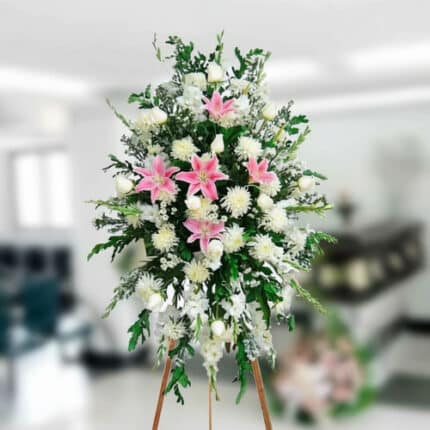 Arreglo floral funerario alto sobre caballete con lirios rosas y flores blancas en interior difuminado