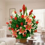 Arreglo de flores con lirios rosados y blancos y rosas rojas en maceta marrón sobre mesa en una sala de estar luminosa