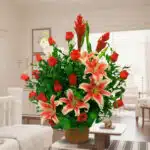 Arreglo de flores con lirios rosados y blancos y rosas rojas en maceta marrón sobre mesa en una sala de estar luminosa