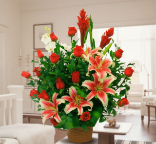 Arreglo de flores con lirios rosados y blancos y rosas rojas en maceta marrón sobre mesa en una sala de estar luminosa