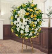 Arreglo floral redondo de pie con rosas amarillas, flores blancas y follaje verde sobre caballete de madera en interior elegante