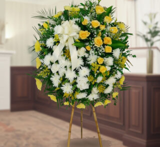 Arreglo floral redondo de pie con rosas amarillas, flores blancas y follaje verde sobre caballete de madera en interior elegante