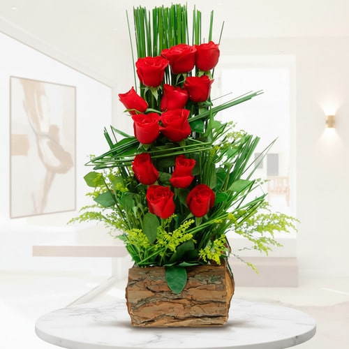 Arreglo vertical de rosas rojas en base de madera rústica arreglo floral vertical con rosas rojas y follaje verde en base de corteza de madera sobre mesa blanca