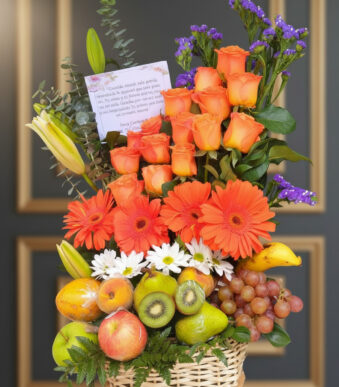 Arreglo floral con rosas y gerberas naranjas, margaritas blancas y flores moradas acompañado de canasta de frutas con manzanas, peras, kiwi, uvas, plátano y otras frutas frescas