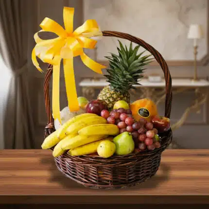 canasta de mimbre con plátanos, uvas, piña, peras y otras frutas variadas decorada con gran lazo amarillo sobre mesa de madera en interior elegante