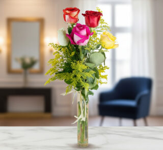 Ramo vertical de rosas rojas, rosas, blancas y amarillas con follaje verde en jarrón de cristal estrecho sobre mesa de mármol, con sala de estar desenfocada al fondo