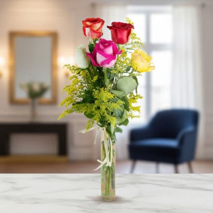 Ramo vertical de rosas rojas, rosas, blancas y amarillas con follaje verde en jarrón de cristal estrecho sobre mesa de mármol, con sala de estar desenfocada al fondo