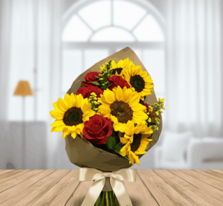 Ramo de flores con girasoles amarillos y rosas rojas envuelto en papel kraft y lazo crema, apoyado sobre mesa de madera con sala luminosa de fondo