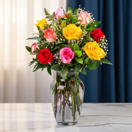 Arreglo floral de rosas rojas, rosas y amarillas con paniculata en jarrón de cristal sobre mesa de mármol