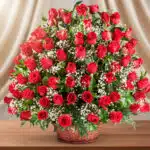 Gran arreglo floral de rosas rojas con flores blancas pequeñas en canasta de mimbre sobre mesa de madera