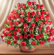 Gran arreglo floral de rosas rojas con flores blancas pequeñas en canasta de mimbre sobre mesa de madera