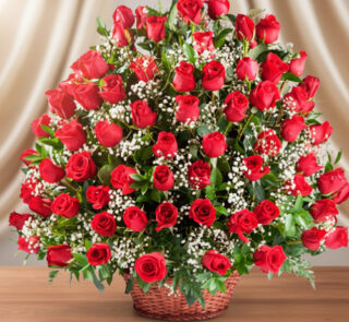 Gran arreglo floral de rosas rojas con flores blancas pequeñas en canasta de mimbre sobre mesa de madera