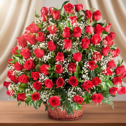 Gran arreglo floral de rosas rojas con flores blancas pequeñas en canasta de mimbre sobre mesa de madera