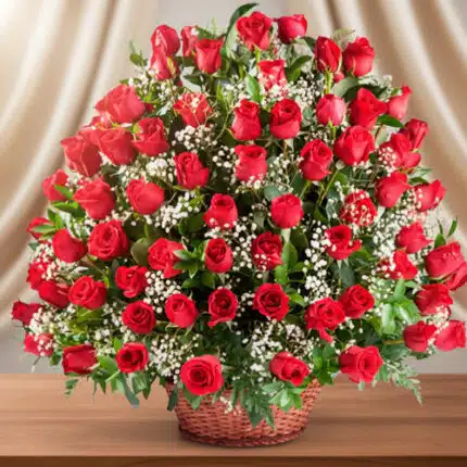 Gran arreglo floral de rosas rojas con flores blancas pequeñas en canasta de mimbre sobre mesa de madera