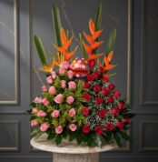 Arreglo floral de cumpleaños con rosas rojas y rosas, aves del paraíso naranjas, follaje verde y globo redondo con texto feliz cumpleaños sobre mesa de mármol
